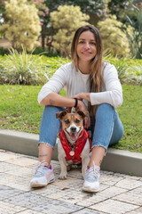 Woman and Jack Russel dog wearing red jacket both smilling to the camera posing on the green grass on a warm summer day