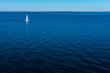 Obraz premium Sail boat far away close to the horizon in the baltic sea. Seen from Kullaberg, a nature reserve and mountain in Skåne, Sweden. Sailboat going to the right with negative space water beneath