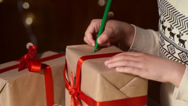 Close up child hand decorate hand made gift box New year present packaging. Making surprise for family. Kid dreaming miracle. Christmas eve holiday fairy lights and ringing bells.