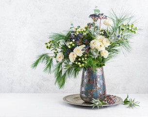 Beautiful winter bouquet in vase. Flower arrangement with roses, fir branches, winter berries,...