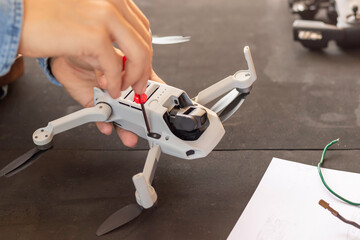 Close up view of unrecognizable man hands repairing small drone with screwdriver in hands in a black tool bank