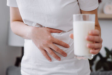 Close up of unhealthy young caucasian female holding glass of milk having bad stomach ache because...