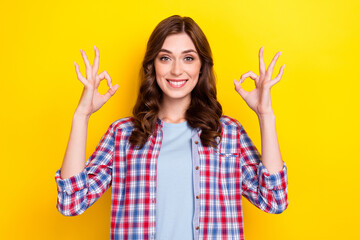 Photo of pretty shiny young girl dressed checkered showing two okey signs isolated yellow color background