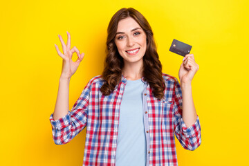 Photo of charming cute girl dressed checkered shirt rising debit card showing okey sign isolated yellow color background