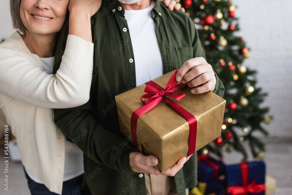 Wall mural cropped view of happy middle aged woman hugging husband with christmas present