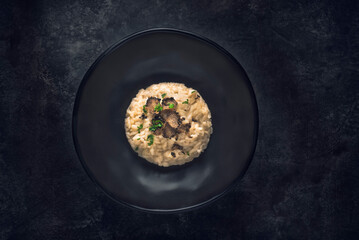 Black truffle risotto recipe.  Autumn creamy consistency risotto in stylish black dish on the black background. Dark autumn or winter mood in the style of the Chef's table, one dish - 543489714
