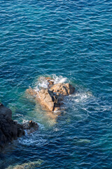 Obraz premium Wild rocky beach coastline and the sea, wave splashes on rock in sea shore, calm sea. Breaking waves to the rocks on shore creating white sea foam and small bubbles, top view