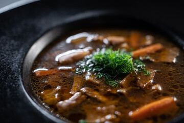 black plate with brown soup pottage with mushroom, carrot, vegetables, dill