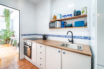 Traditional bright kitchen with white cabinets and blue tiles. Spacious modern fully equipped appliance interior with wooden desk, ceramic stove and a patio