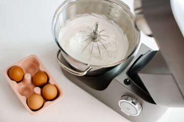 On the table is a mixer with white meringue cream inside. Homemade sweets. High quality photo