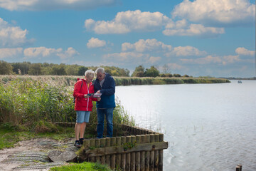 Middle aged couple studying their map as they walk by the Norfolk Broads in East Anglia UK enjoying the sunny Autumn weather and exercising together.