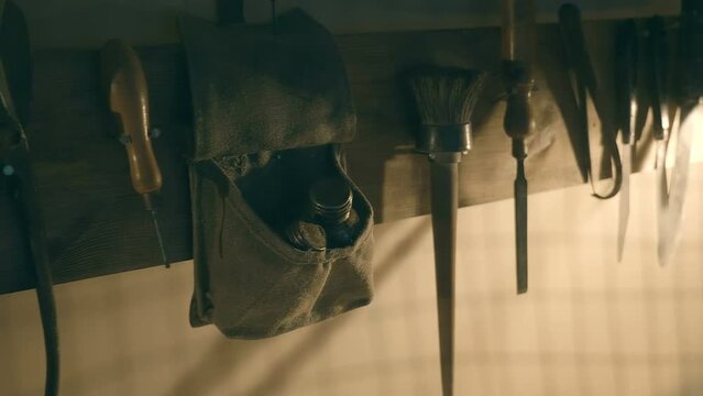 In the twilight, tools on the wall on wooden plank of an ancient archaeologist, explorer, adventurer on which a file, metal scissors, an awl, a brush, a chisel, knives, wire cutters and a bag