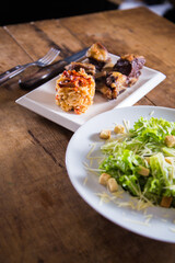 A gaucho traditional carreteiro rice and barbecue meat dish next to a fresh healthy caesar salad in white plates onto a wooden rustic table ready for lunch or dinner