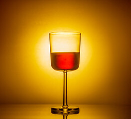 A glass of red wine on a glowing orange background is reflected in a mirror table