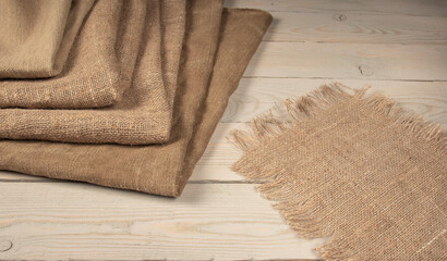 A stack of coarse peasant cloth - burlap and a tarpaulin on a wooden table. Rustic style image - obrazy, fototapety, plakaty