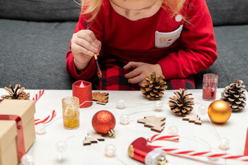 Little child wearing christmas holiday pajamas, doing crafts Christmas tree decorations.