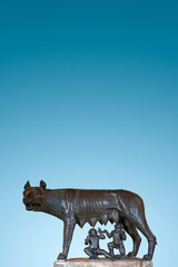 Cover page with a monument of a mother wolf feeding enfants, Romulus and Remus at Rome, Italy, with copy space and blue sky gradient background.