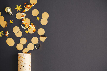 Modern golden confetti popping from festive wrapping paper on black background, new year firework...