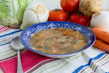 Top close up view of a plate of minestrone with tomatoes, potatoes, fennel, cabbage, carrots, onion...