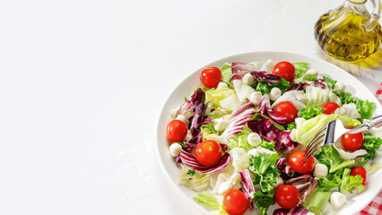 Fresh salad with green leaves mix, cherry tomatoes and cheese on a white plate with olive oil on a white background with copy space. Healthy dieting food. Cooking and eating at home