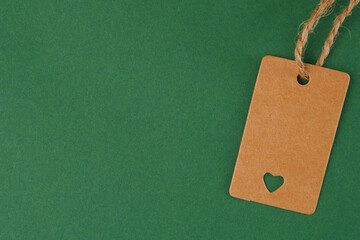 An empty price tag, a gift label template or a kraft paper label with a heart and a jute cord on a green background.Minimalistic shopping concept, Black Friday, Christmas sales.Copyspace
