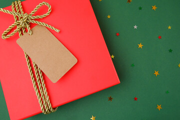 A red gift box tied with a golden tourniquet with an empty label on a green background with stars. A Christmas present.Packaging, sale of gifts. Copyspace