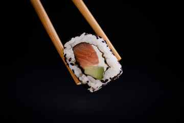 salmon cheese and avocado uramaki roll held by chopsticks on a black background © Sergio