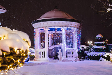 Illuminated gazebo lights winter night snow on ground. Holiday gazebo. Christmas Lights outside on...
