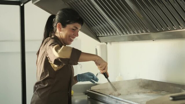 Woman smiling while using a spatula to clean the griddle in the restaurant kitchen.