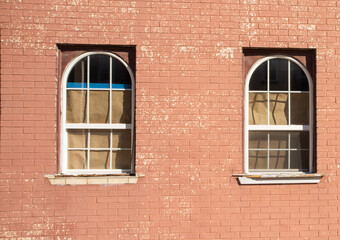Old red brick building with two arched windows with brown paper on the inside so you can't see...