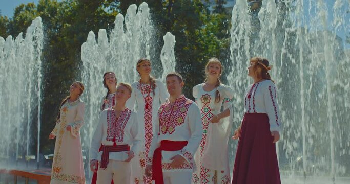Ukrainian women and men in national folk costumes with embroidery are talking in the park, they are happy. Ukrainian people walk in the park, friendship of peoples. 4k, ProRes