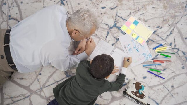 Father and son draw pictures and do homework at home.
Father helps his son with homework and they spend time together.

