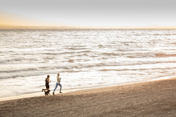 Dos chicas corriendo por una playa de Málaga al atardecer.