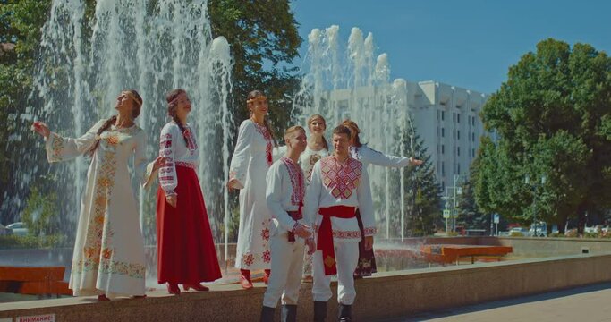 Slavic men and women in beautiful national costumes sing and rejoice in the city park. Slavic people are happy, men and women are smiling. Men and women are dressed in traditional Slavic costumes