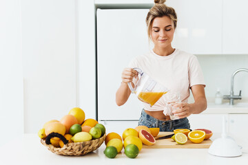 Woman pouring freshly squeezed homemade orange juice into the glass in modern white kitchen