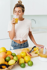 Obraz premium Woman drinking freshly squeezed homemade orange juice in white kitchen