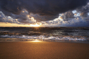 a beach with waves and a cloudy sky above it and the sun setting in the distance with a boat in the...