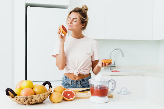 Beautiful woman sniffing fresh grapefruit during citrus juice preparation at home