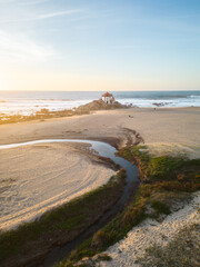 Aerial views of Senhor da Pedra Church at sunset, in the middle of the beach and ocean at Miramar, Portugal
