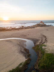 Aerial views of Senhor da Pedra Church at sunset, in the middle of the beach and ocean at Miramar, Portugal