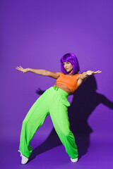 Fototapeta na wymiar Active woman dancer wearing colorful sportswear performing against purple background