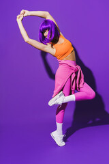Carefree woman dancer wearing colorful sportswear performing against purple background