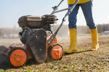 Woman villager is using aerator machine to scarification and aeration of lawn or meadow