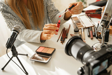 Female hands with lipstick brush applicator. Woman beauty blogger making a video review of cosmetic...