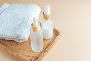 Skin care set in frosted glass bottles on wooden tray with towels. Beauty treatment routine mockup. Spa concept