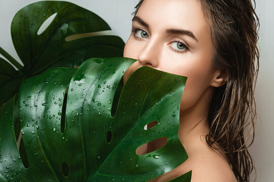 Young woman with a smooth skin holding Monstera deliciosa plant leaf