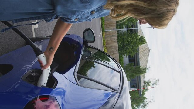 Vertical video of woman outdoors detaching charging cable from electric car - shot in slow motion
