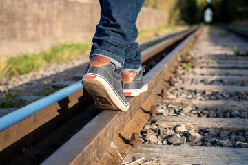 Hombre caminando en las vías del tren, haciendo equilibrio. Fotografía con enfoque selectivo en...