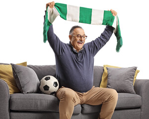 Mature man sitting on a sofa and cheering with a scarf