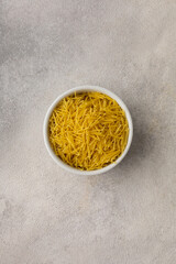 White bowl with yellow vermicelli on a light background